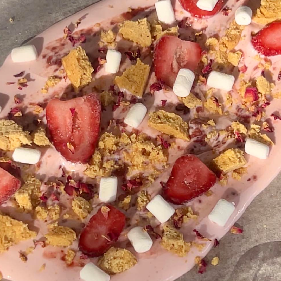 Pink High Protein Ambrosia Yogurt Bark with strawberry yogurt, strawberry slices, potein cookie chunks, mini marshmallows and dried rose petals